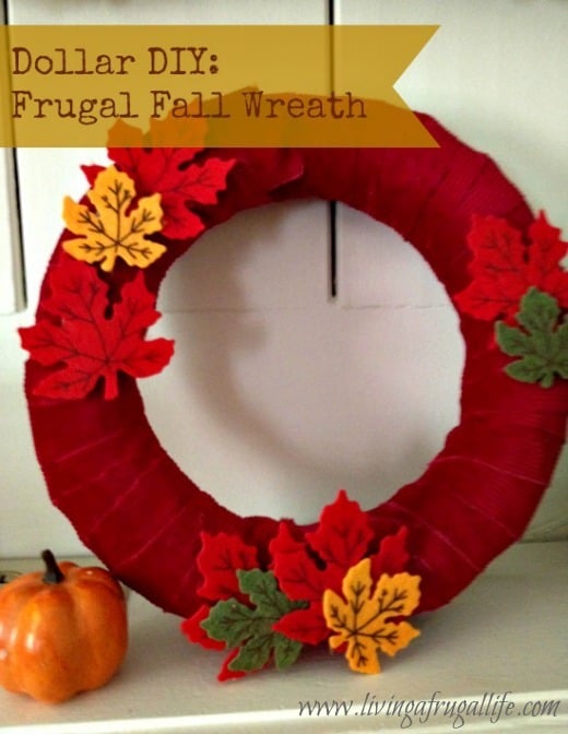 red ribbon wrapped fall wreath with fall colored leaves and a pumpkin. all purchased from the dollar store