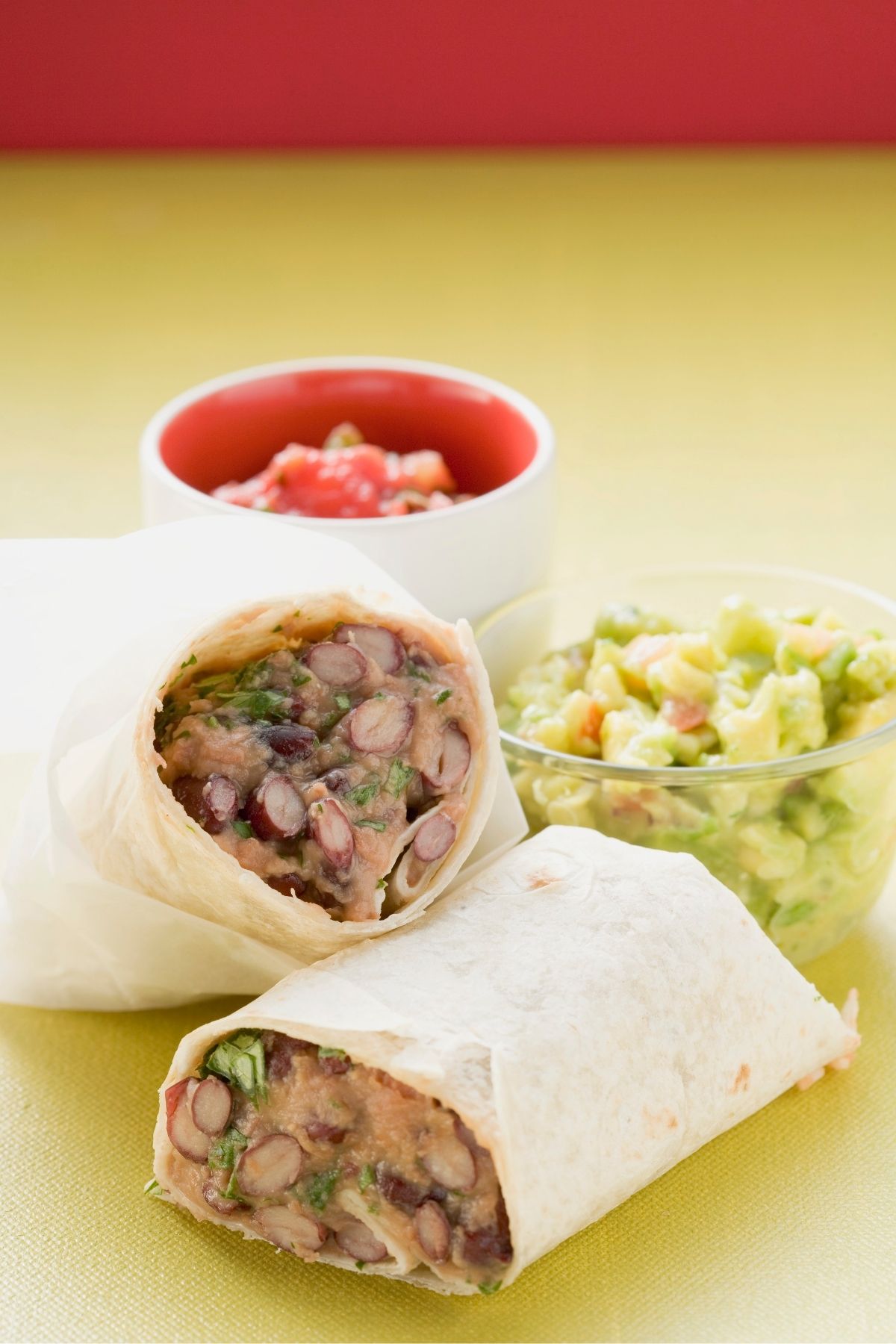 Freezer bean burrito cut in half next to salsa and lettuce.