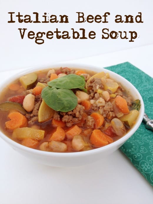 white background with white bowl of italian beef and vegetable soup. soup has carrots, white beans, ground beef, zuchinni and yellow squash in it. Has text overlay that says Italian Beef And Vegetable Soup.