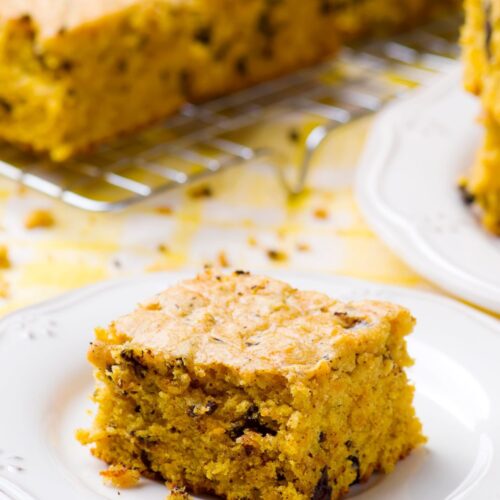 Slice of pumpkin squares recipe on a white plate with the other pieces of pumpkin bar behnd them.