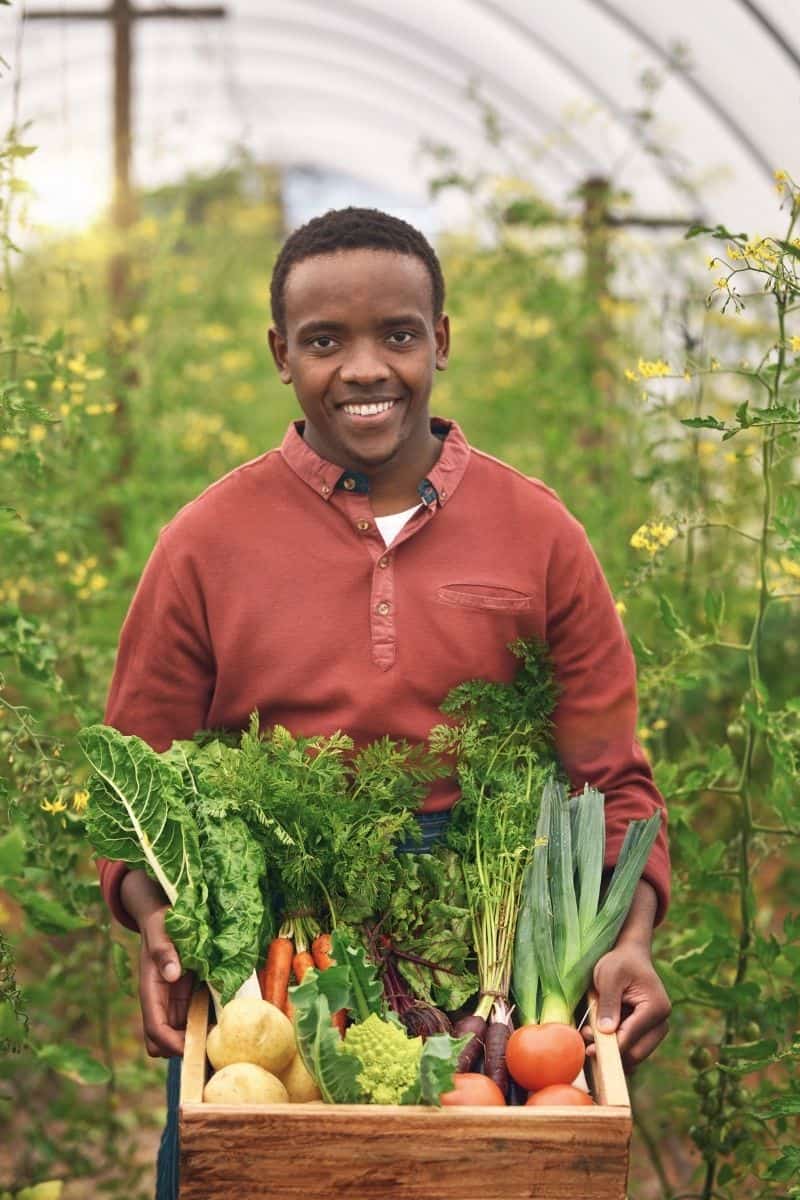 Man holding a produce box in a garden.