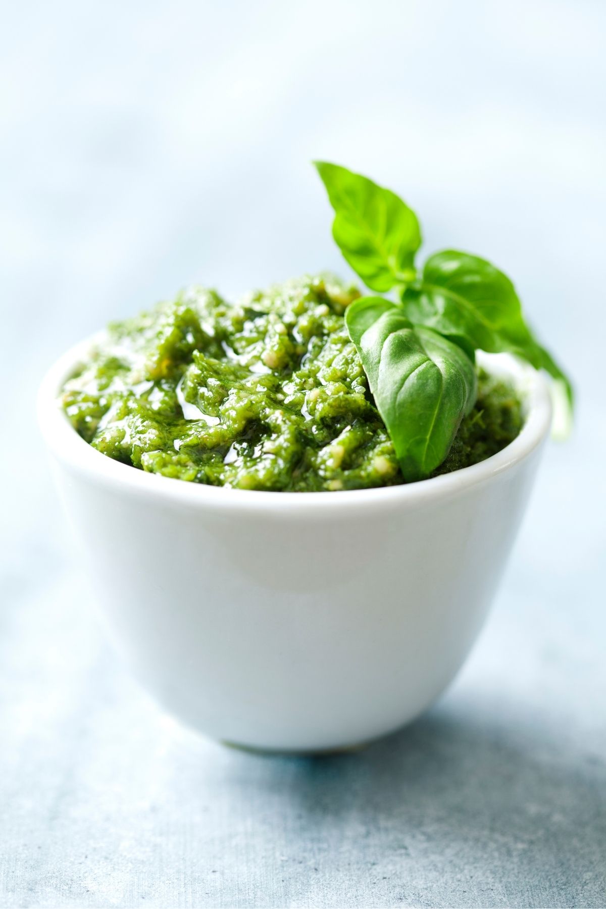 White bowl with homemade pesto in it. topped with a basil leaf.